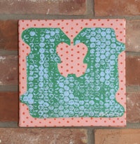 a green and pink polka dot tile hanging on a brick wall